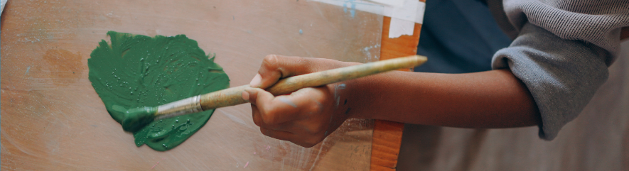 Boy holding paintbrush, painting green paint onto cardboard