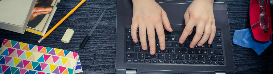 Hands on a laptop keyboard, surrounding by school supplies