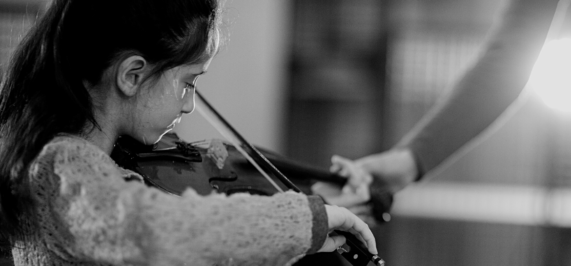 Young girl playing violin as teacher guides her