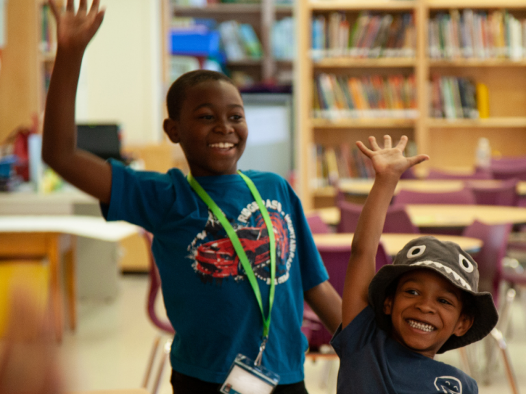 Two boys wave their hands with excitement in a library